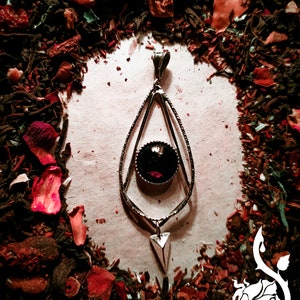 Puede incluir: Un colgante de plata con una piedra preciosa negra en un diseño geométrico. El colgante está rodeado de pétalos de flores rojas y marrones.