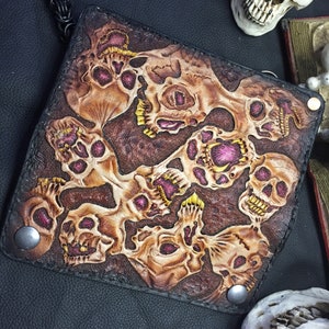 May include: A black leather wallet with a skull design. The wallet is decorated with multiple skulls in shades of brown, pink, and yellow.