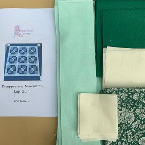 May include: A quilt kit for a disappearing nine patch lap quilt. The kit includes fabric in green, cream, and a floral print. The kit also includes instructions for the quilt.