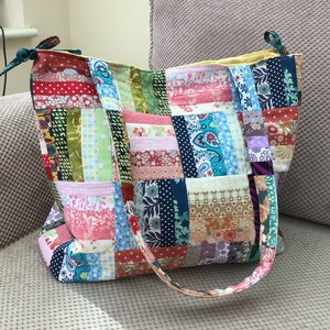 Peut inclure: Un sac fourre-tout en patchwork avec une vari&eacute;t&eacute; de tissus color&eacute;s, y compris des motifs floraux, paisley et g&eacute;om&eacute;triques. Le sac a deux longues lani&egrave;res et une fermeture &agrave; cordon.
