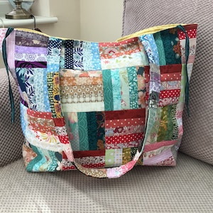 Peut inclure: Un sac fourre-tout en patchwork avec une doublure jaune et des sangles vertes. Le sac est fait de diff&eacute;rents tissus color&eacute;s avec des motifs floraux et g&eacute;om&eacute;triques.