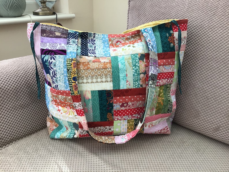 Peut inclure: Un sac fourre-tout en patchwork avec une doublure jaune et des sangles vertes. Le sac est fait de diff&eacute;rents tissus color&eacute;s avec des motifs floraux et g&eacute;om&eacute;triques.