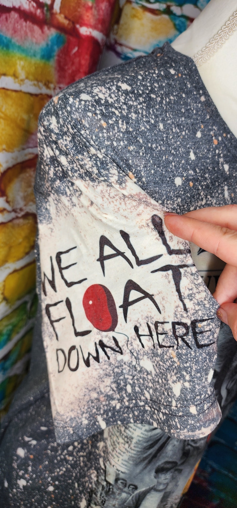 May include: A gray and white t-shirt with the text "WE ALL FLOAT DOWN HERE" and a red balloon graphic. The shirt has a distressed, speckled design.