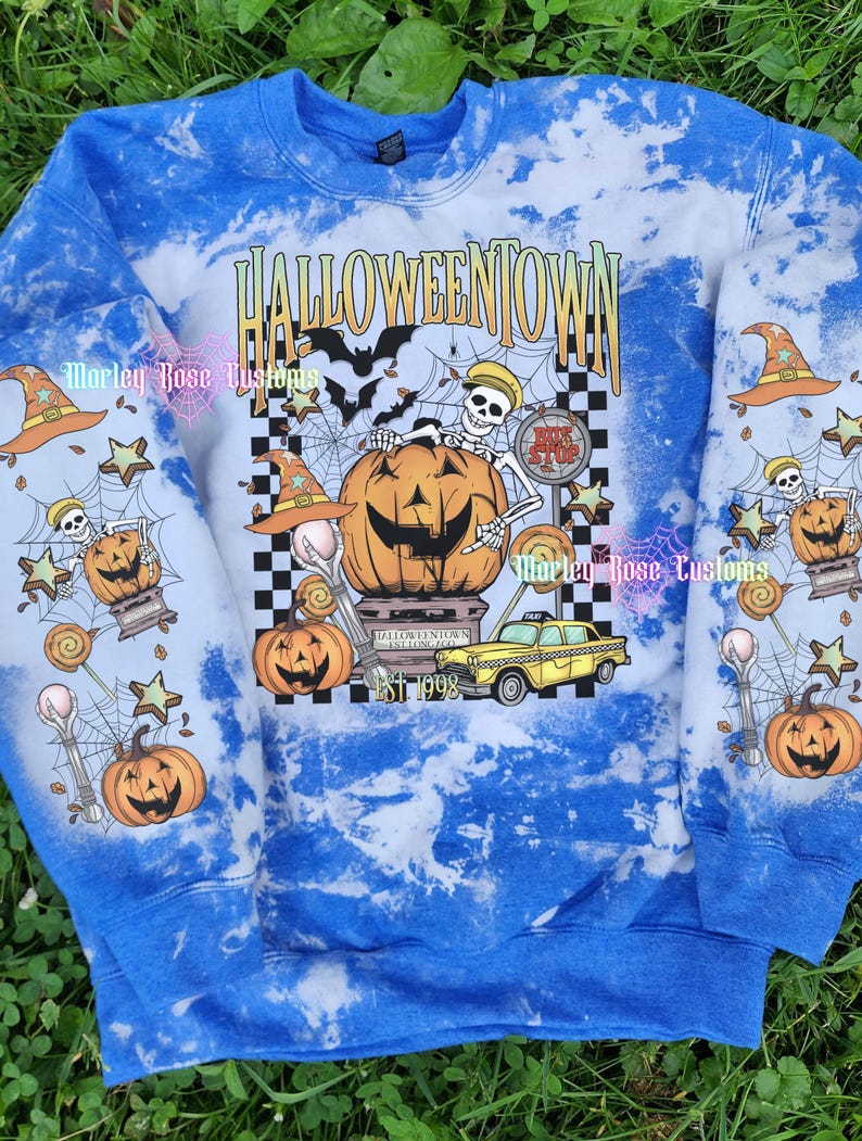 May include: A blue and white tie-dye sweatshirt featuring a graphic print with the text HALLOWEENTOWN EST 1998. The design includes a skeleton, a large jack-o'-lantern, a yellow taxi, bats, spiderwebs, witch hats, and lollipops on the front and sleeves.