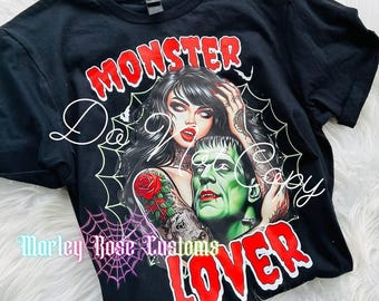 May include: Black t-shirt with a graphic featuring a woman and Frankenstein's monster. The words "MONSTER LOVER" are in red, and the design includes a spiderweb and a rose tattoo.