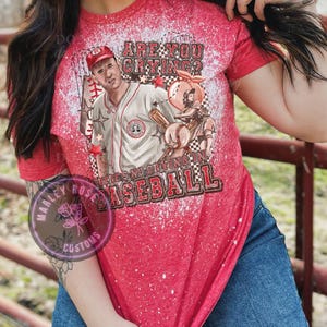 May include: Red, white, and blue bleached t-shirt with a baseball player graphic and the text "Are you crying? There's no crying in baseball."