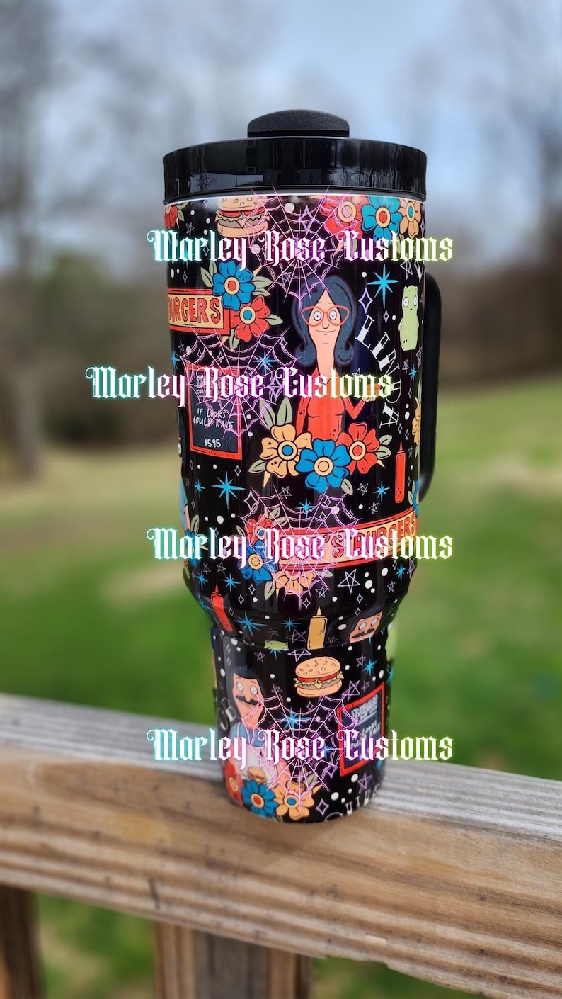 May include: A white ceramic mug with a black handle and the text "But First, Coffee" in a bold, black font. The mug is set against a blurred background, suggesting a cozy setting.
