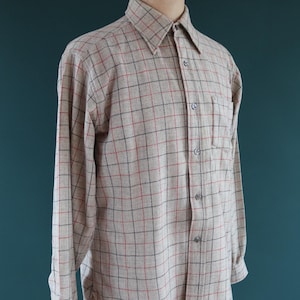 May include: A long-sleeved button-down shirt in a beige and red plaid pattern. The shirt has a classic collar, a chest pocket, and is displayed on a mannequin. The plaid pattern features thin red and black lines.