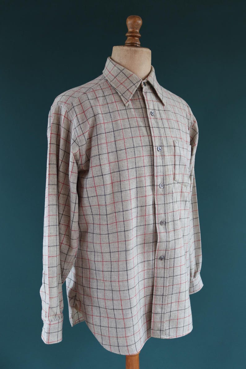 May include: A long-sleeved button-down shirt in a beige and red plaid pattern. The shirt has a classic collar, a chest pocket, and is displayed on a mannequin. The plaid pattern features thin red and black lines.