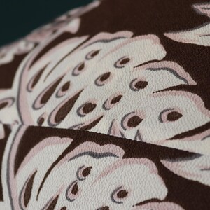 Peut inclure: Gros plan sur un tissu brun avec un motif floral blanc. Le tissu a une surface textur&eacute;e et les fleurs sont d&eacute;taill&eacute;es avec de petits points blancs.
