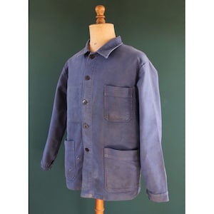 May include: A blue work jacket with three front pockets and button closures. The jacket is displayed on a mannequin against a green background. The jacket has a collar and long sleeves.