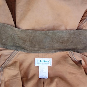 May include: Close-up of a tan-colored jacket with a corduroy collar. The jacket has a label that reads "L.L.Bean Freeport, Maine". The collar is a darker shade of brown than the jacket. The jacket is made of a durable material.