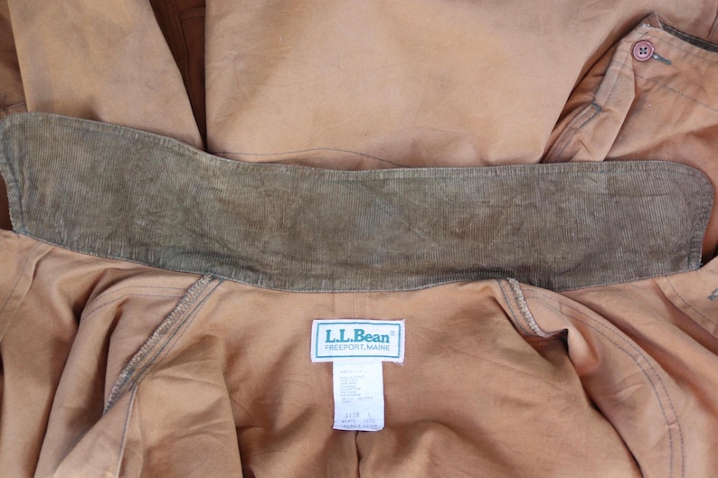 May include: Close-up of a tan-colored jacket with a corduroy collar. The jacket has a label that reads "L.L.Bean Freeport, Maine". The collar is a darker shade of brown than the jacket. The jacket is made of a durable material.