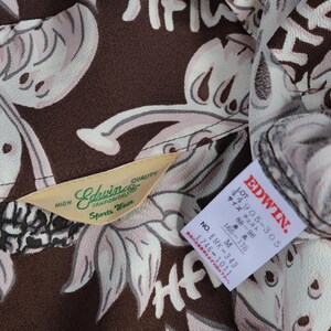 Peut inclure: Tissu &agrave; motifs marrons et blancs avec une &eacute;tiquette indiquant "Edwin Sports Wear" et une autre &eacute;tiquette indiquant "EDWIN. 1905-305 88-96 サイズ チェスト 165-175 M NO EMK-343 1746-1011"