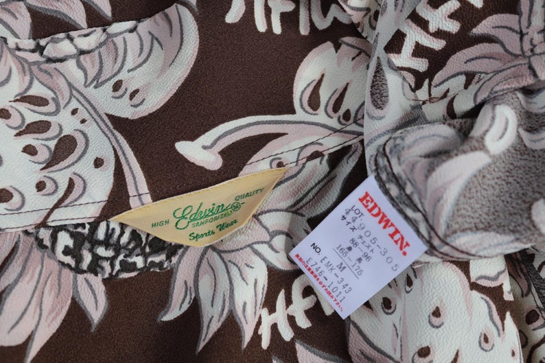 Peut inclure: Tissu &agrave; motifs marrons et blancs avec une &eacute;tiquette indiquant "Edwin Sports Wear" et une autre &eacute;tiquette indiquant "EDWIN. 1905-305 88-96 サイズ チェスト 165-175 M NO EMK-343 1746-1011"