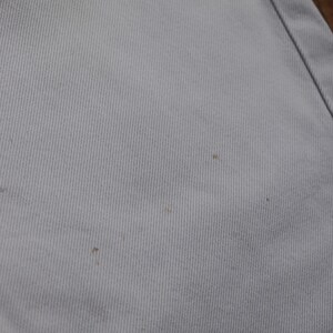 May include: Close-up of a light gray fabric with a subtle texture. There are three small brown spots on the fabric.