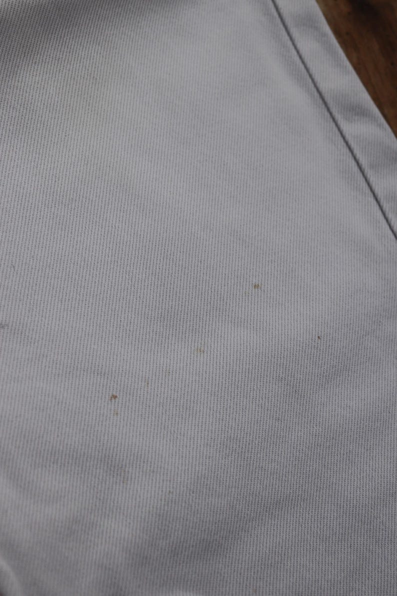 May include: Close-up of a light gray fabric with a subtle texture. There are three small brown spots on the fabric.