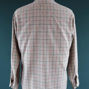 May include: A long-sleeved shirt displayed on a mannequin. The shirt is a light beige color with a plaid pattern of red and black lines. The shirt has a button-down collar and buttoned cuffs.