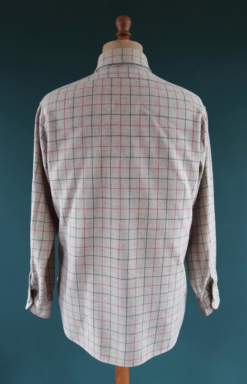 May include: A long-sleeved shirt displayed on a mannequin. The shirt is a light beige color with a plaid pattern of red and black lines. The shirt has a button-down collar and buttoned cuffs.