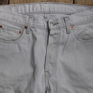 May include: A pair of light gray denim jeans with a classic five-pocket style. The jeans have a straight leg and a button fly.