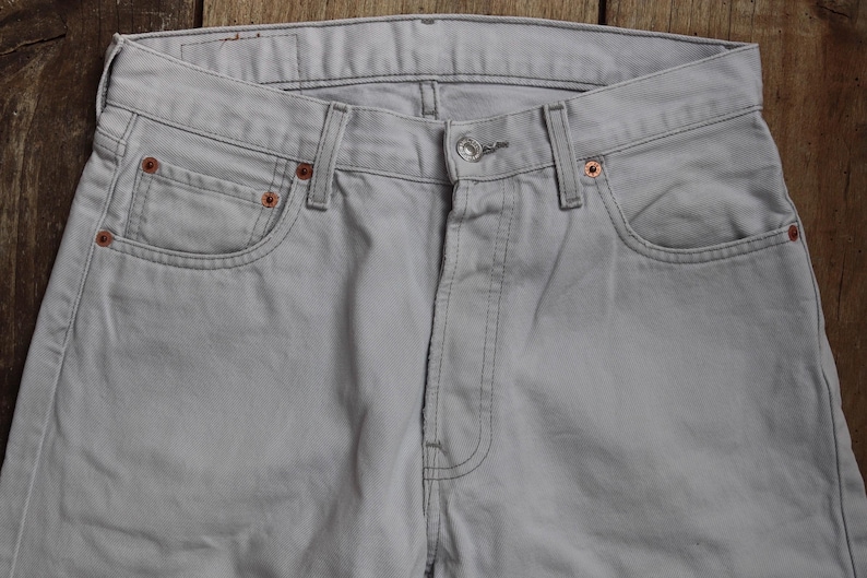 May include: A pair of light gray denim jeans with a classic five-pocket style. The jeans have a straight leg and a button fly.
