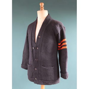 May include: Navy blue cardigan sweater with orange stripes on the left sleeve. The sweater has a shawl collar, two front pockets, and button closures. The sleeves are cuffed at the wrists.