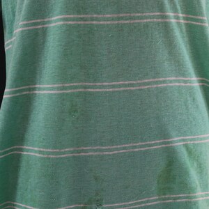May include: Green and white striped t-shirt. The shirt has horizontal stripes and appears to be made of a soft, worn fabric. The shirt has some stains and a small hole.