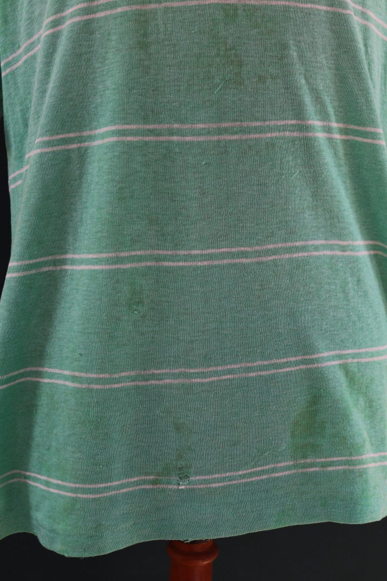 May include: Green and white striped t-shirt. The shirt has horizontal stripes and appears to be made of a soft, worn fabric. The shirt has some stains and a small hole.