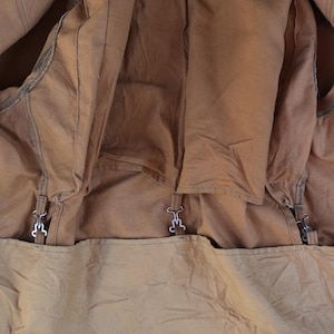 May include: Close-up of the interior of a brown canvas jacket. The jacket has a light brown lining and metal clasps. The L.L.Bean label is visible at the top. The jacket appears to be well-worn.