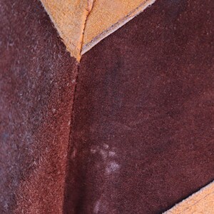 May include: Close-up of a brown leather material with a tan leather border. The leather has a textured, suede-like finish.
