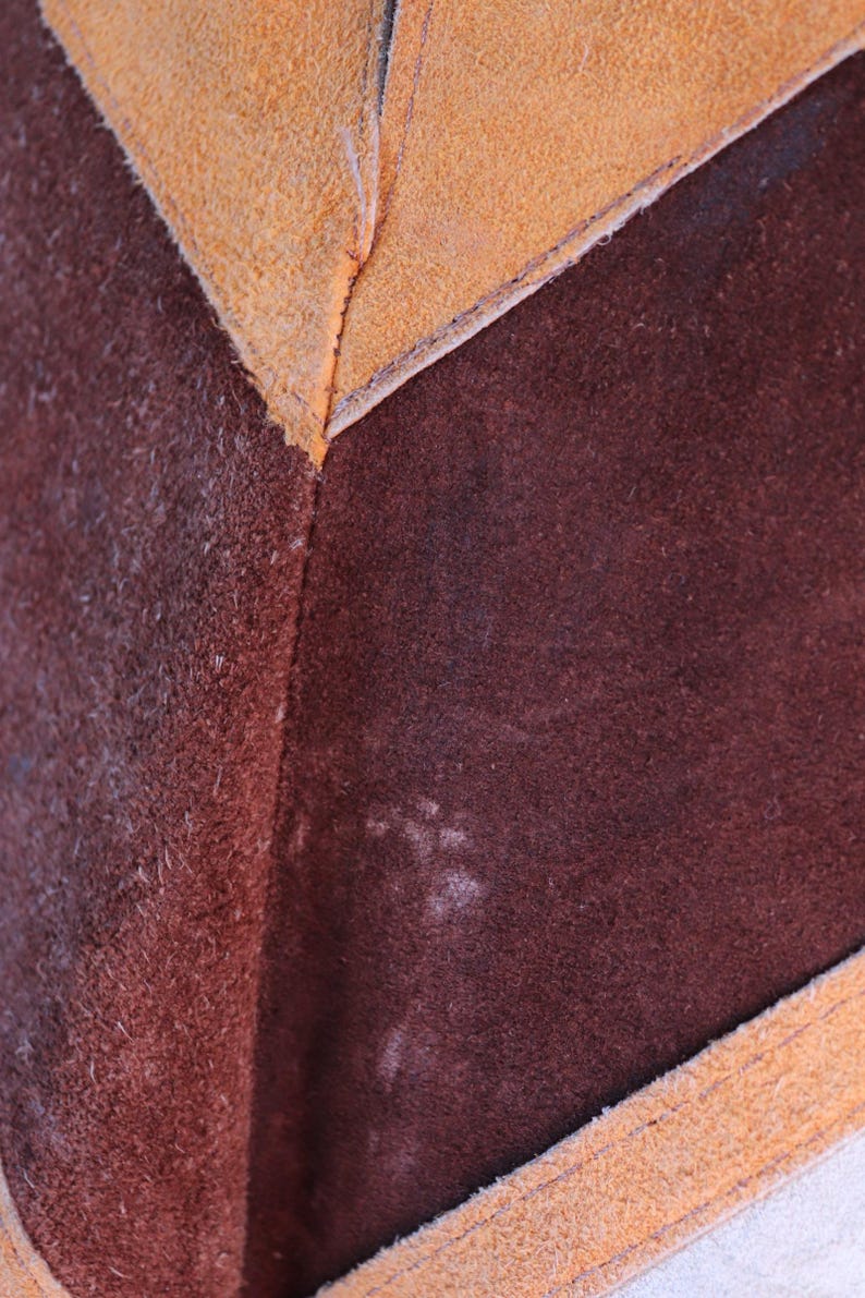 May include: Close-up of a brown leather material with a tan leather border. The leather has a textured, suede-like finish.