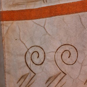 May include: Close-up of a beige fabric with a brown stripe and brown swirl designs. The fabric has a textured surface.
