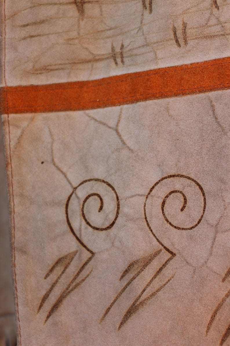 May include: Close-up of a beige fabric with a brown stripe and brown swirl designs. The fabric has a textured surface.