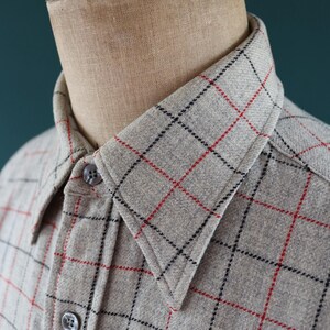 May include: A light gray button-down shirt with a plaid pattern of black and red lines. The shirt is displayed on a mannequin. The collar and button details are visible. The fabric appears to be a soft, woven material.