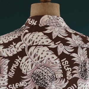 Peut inclure: Chemise boutonn&eacute;e marron &agrave; imprim&eacute; tropical avec des ananas, des feuilles et le texte "Island" et "High My" r&eacute;p&eacute;t&eacute; sur tout le motif.