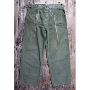 Peut inclure: Pantalon de travail vintage vert olive avec braguette boutonnée et plusieurs poches. Le pantalon présente des signes d'usure, avec des zones décolorées et une coupe décontractée. Le pantalon a une taille haute et une jambe large.