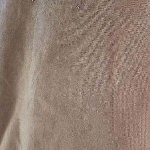 May include: Close-up of a textured, tan fabric with visible imperfections. The fabric has a slightly wrinkled appearance and a subtle sheen. Small, irregular marks are scattered across the surface.