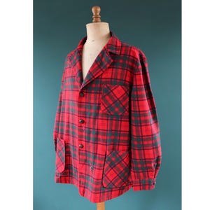 May include: A red and green plaid jacket with a classic design. The jacket features a notched collar, two front pockets, and black buttons. The garment is displayed on a mannequin, showcasing its tailored fit and vintage style.