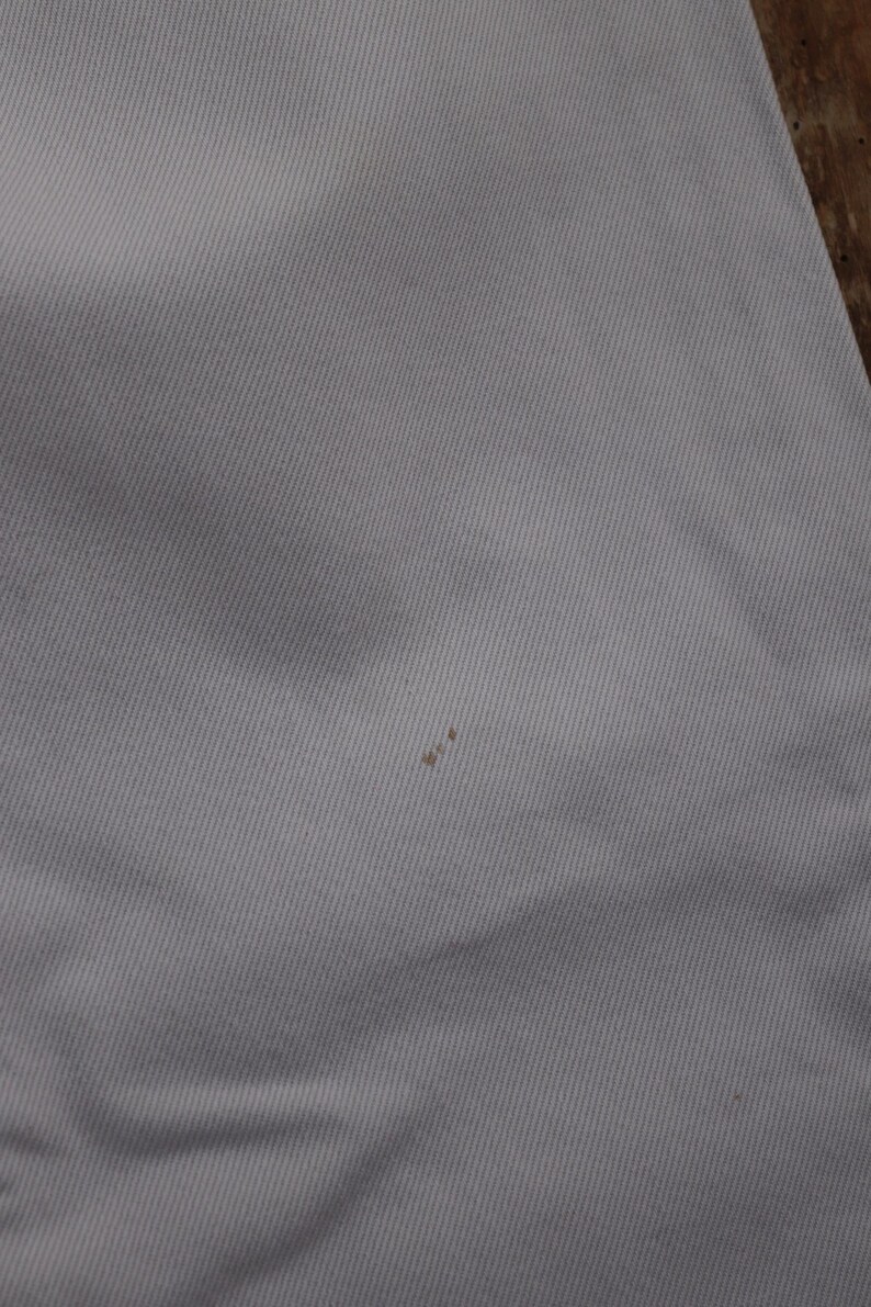 May include: A close-up of a white fabric surface with a small brown stain.
