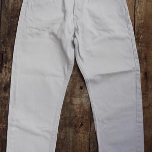 May include: A pair of light gray denim jeans with a straight leg fit. The jeans have a classic five-pocket design and a button fly.