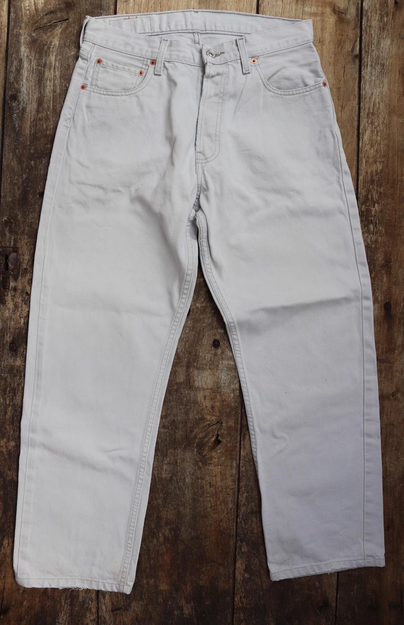 May include: A pair of light gray denim jeans with a straight leg fit. The jeans have a classic five-pocket design and a button fly.