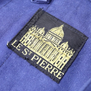 May include: A black patch with gold embroidery of a building and the text "LES ST PIERRE".