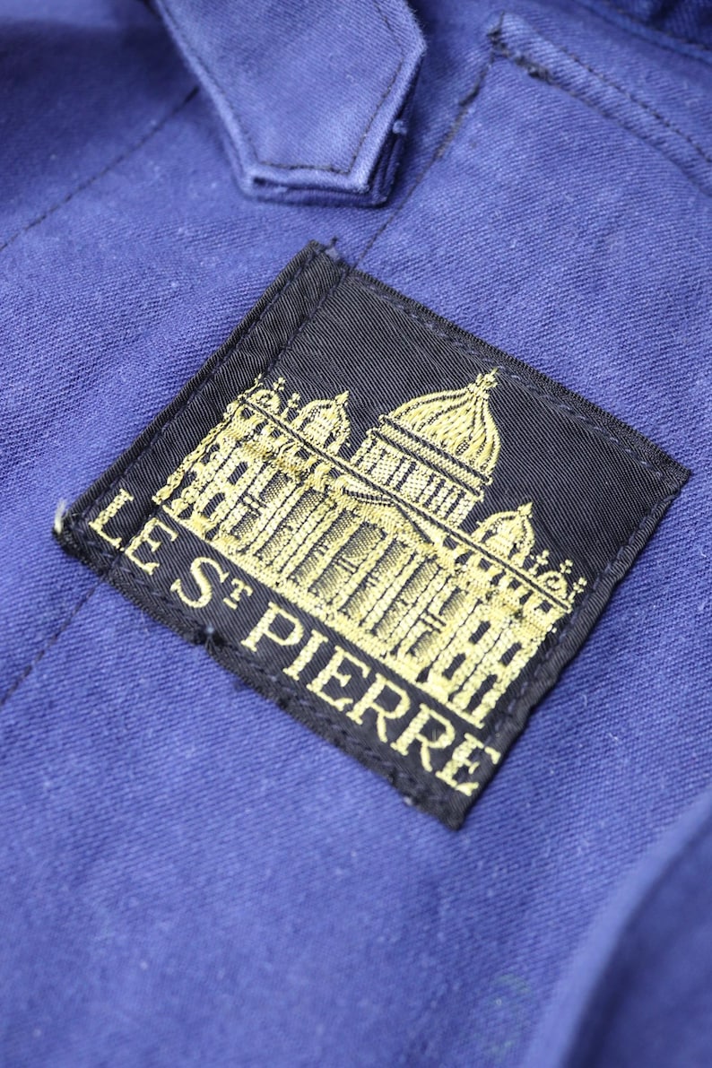 May include: A black patch with gold embroidery of a building and the text "LES ST PIERRE".