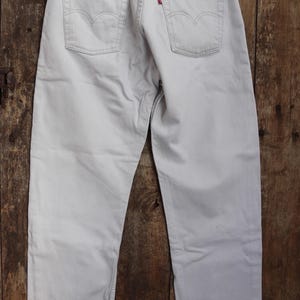 May include: A pair of light gray denim jeans with a brown leather patch on the back pocket that says "Levi's" in red lettering.