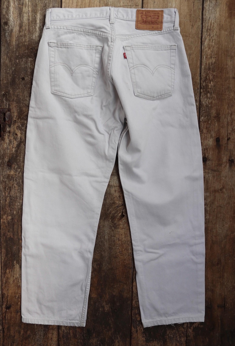 May include: A pair of light gray denim jeans with a brown leather patch on the back pocket that says "Levi's" in red lettering.
