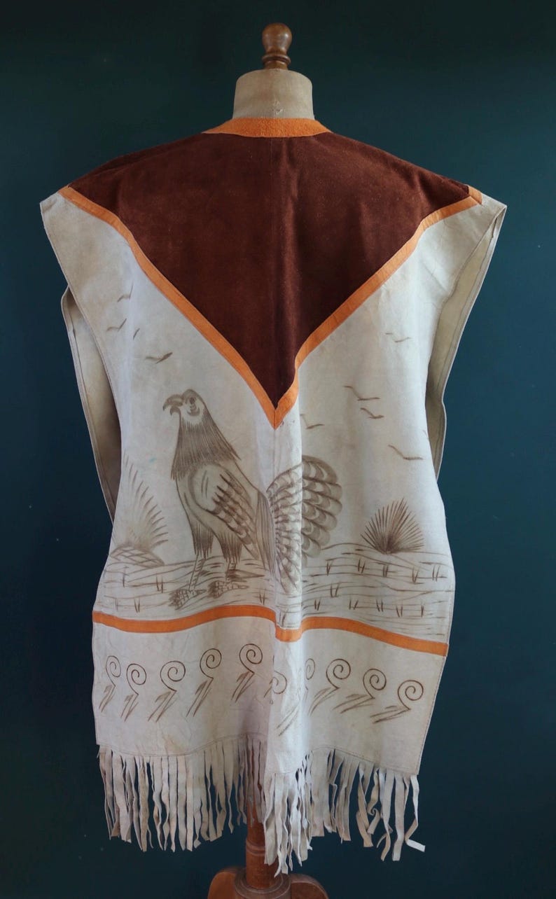 May include: A white leather vest with a brown suede panel and orange trim. The vest features a painted design of a bird with a long tail and a decorative border of swirls. The vest has fringe along the bottom.