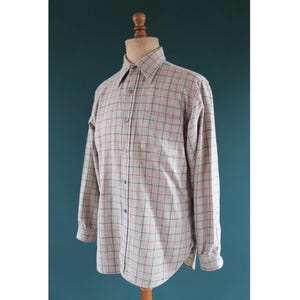 May include: A long-sleeved button-down shirt in a beige and red plaid pattern. The shirt is displayed on a wooden mannequin. The shirt has a classic collar and buttoned cuffs. The fabric appears to be a medium-weight woven material.