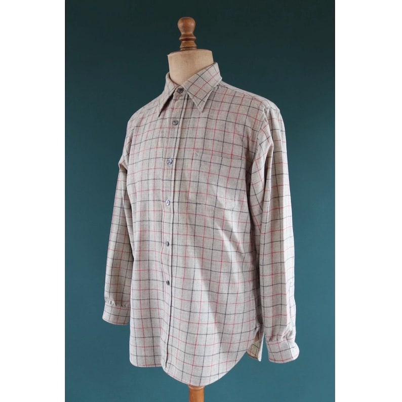 May include: A long-sleeved button-down shirt in a beige and red plaid pattern. The shirt is displayed on a wooden mannequin. The shirt has a classic collar and buttoned cuffs. The fabric appears to be a medium-weight woven material.