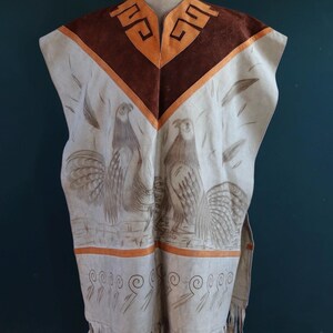 May include: A white leather poncho with brown suede accents and a fringe trim. The poncho features a geometric design at the neckline and two stylized birds in the center.