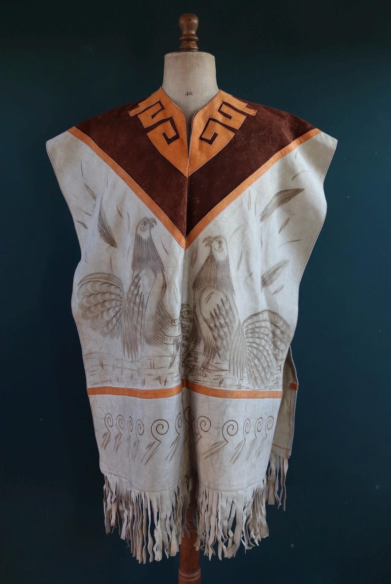 May include: A white leather poncho with brown suede accents and a fringe trim. The poncho features a geometric design at the neckline and two stylized birds in the center.